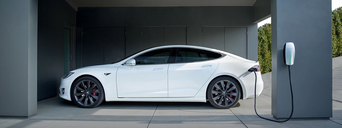 White electric vehicle parked beside a wall-mounted home charging station